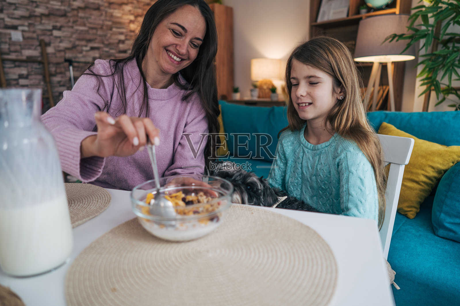 一位快乐的母亲和女儿坐在餐桌旁，一起享用早餐。她们在享受美食，晨光温柔地洒满整个房间。照片摄影图片