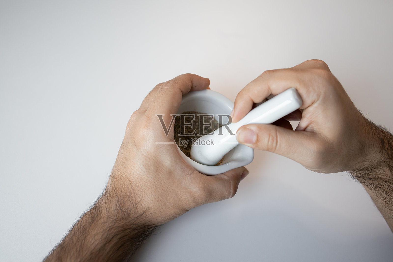 手握白色研钵和杵在白色表面上研磨香料照片摄影图片