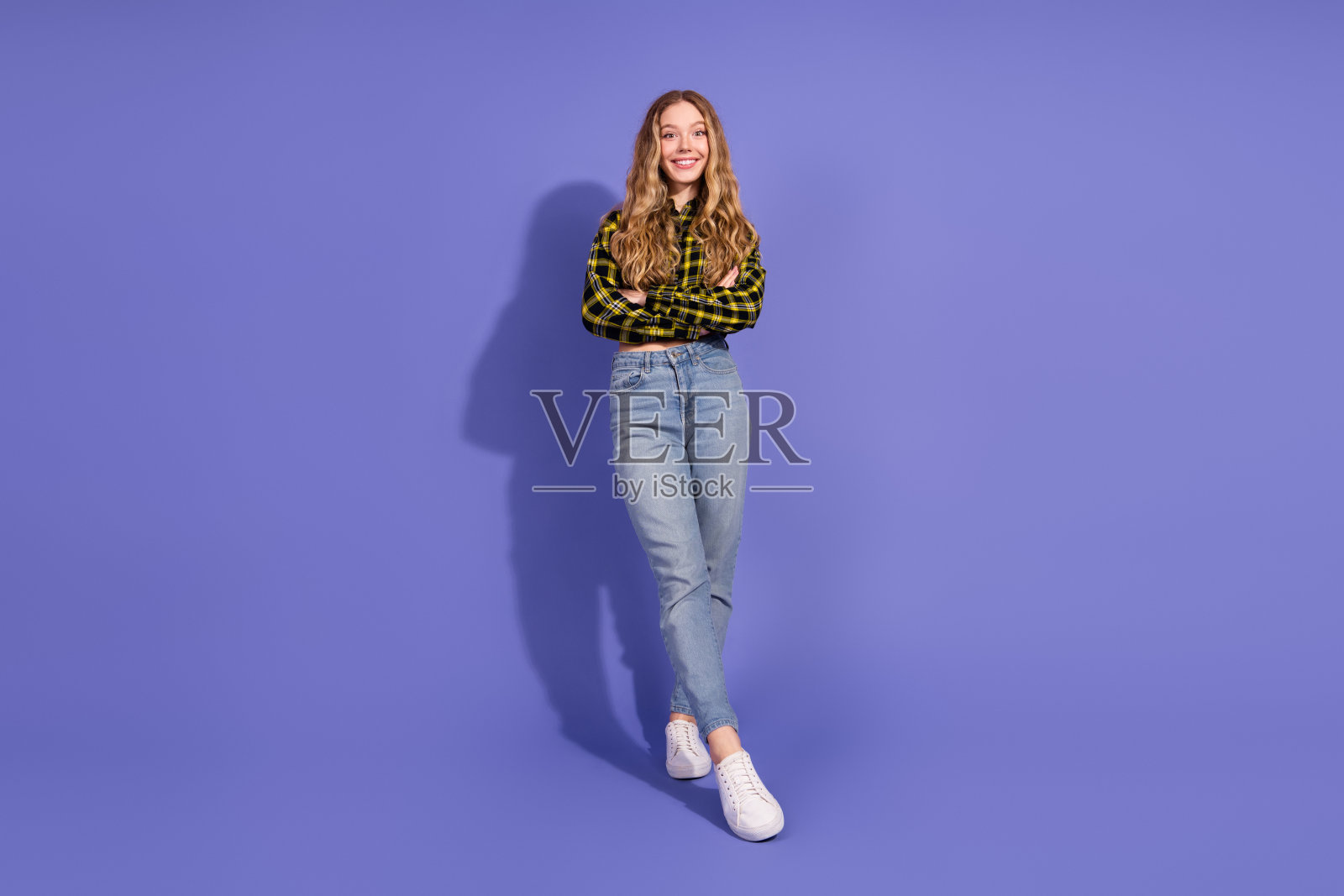 年轻的金发女性穿着休闲的格子衬衫和牛仔裤，自信地站在紫色背景前。照片摄影图片