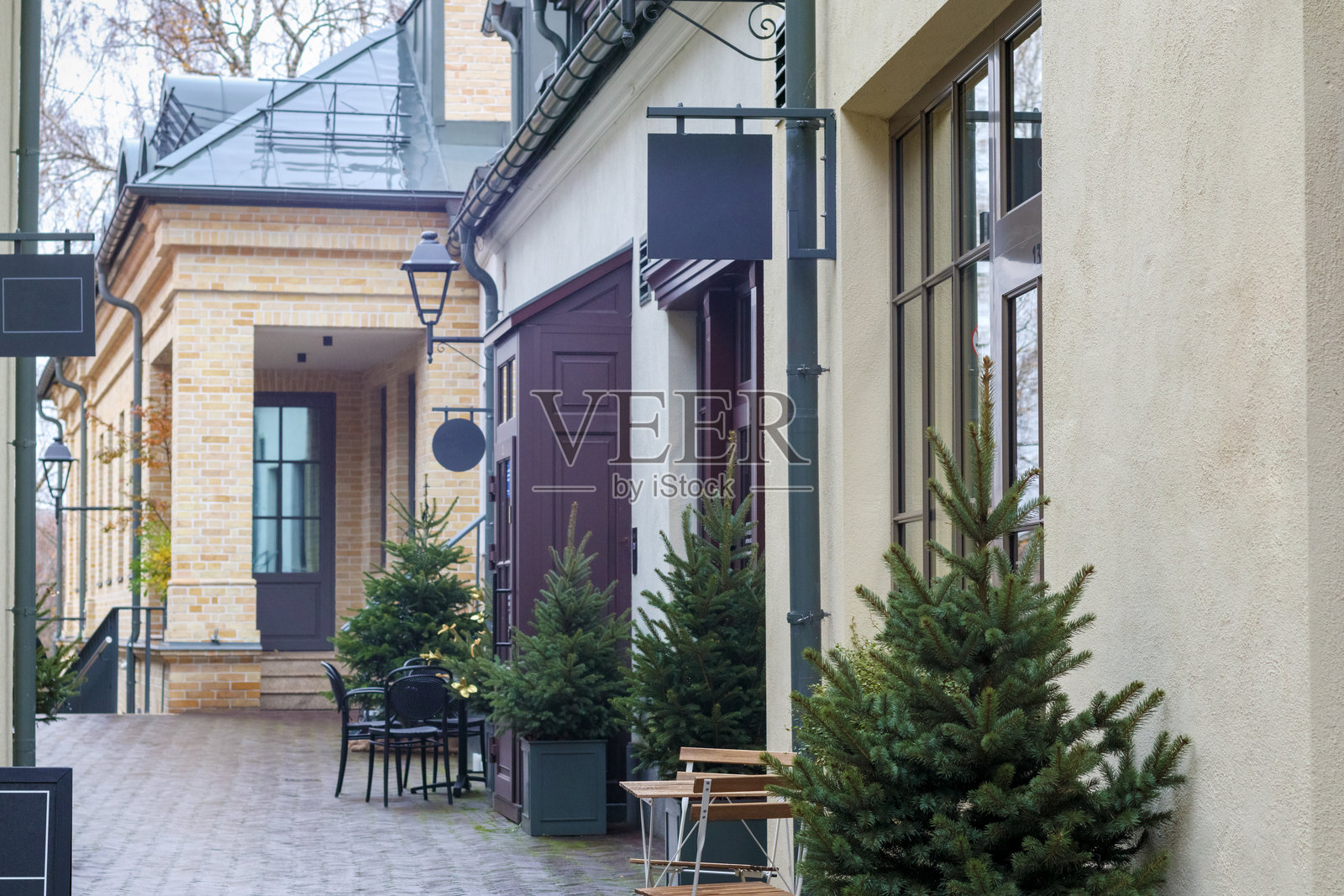 一条狭窄的街道，木质露台上种着盆栽圣诞树，旁边有小桌子和椅子。照片摄影图片
