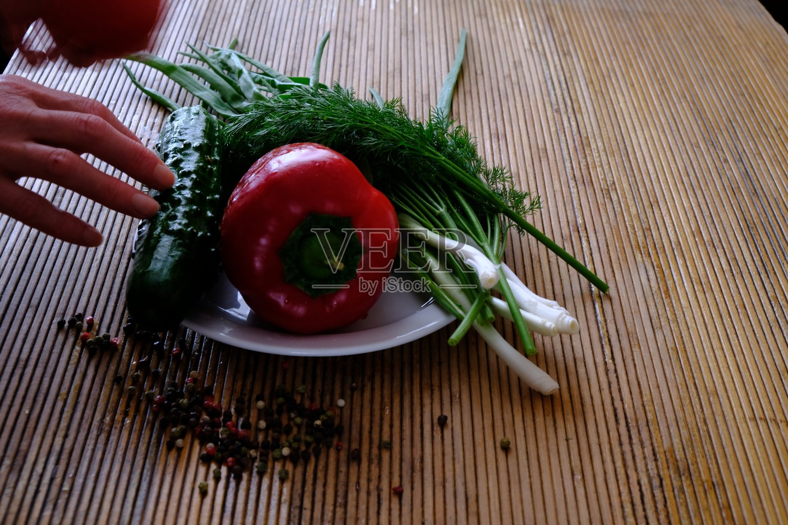 在家中，女人在桌子上准备沙拉，手中拿着不同的蔬菜和香菜，展现出亲密的氛围。照片摄影图片