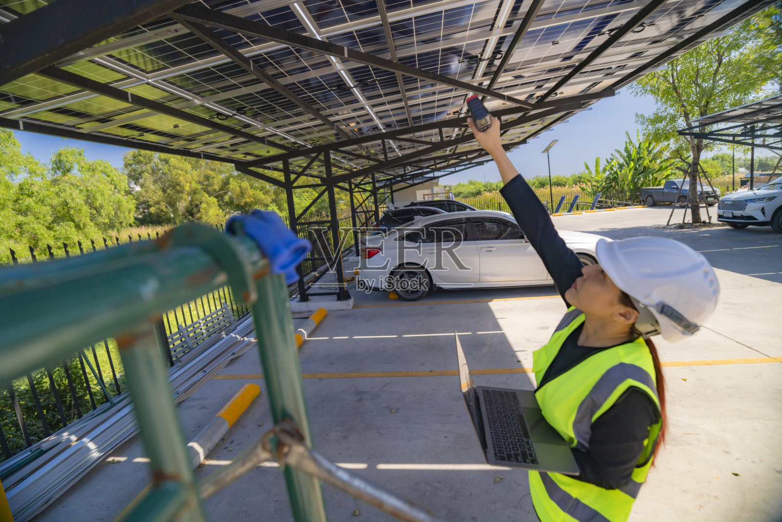 女性工程师在车棚上检查太阳能电池板，同时手持笔记本电脑和红外线温度计。太阳能检查、可再生能源技术和清洁能源基础设施。照片摄影图片