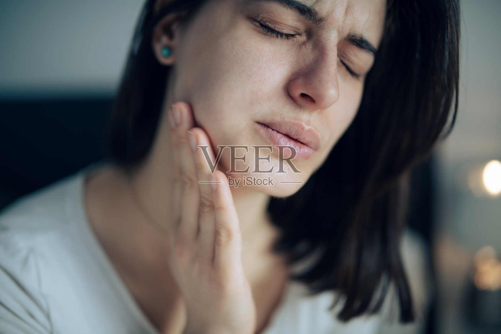 年轻女性因牙痛而捂着脸颊。照片摄影图片