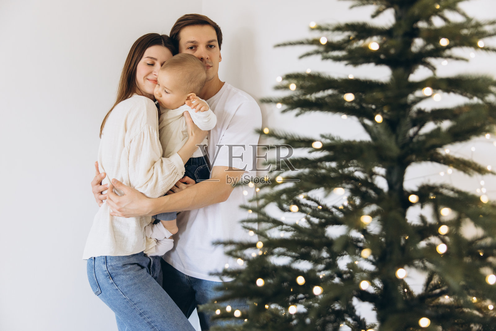 一家人在圣诞树旁拥抱，周围挂满了小彩灯照片摄影图片