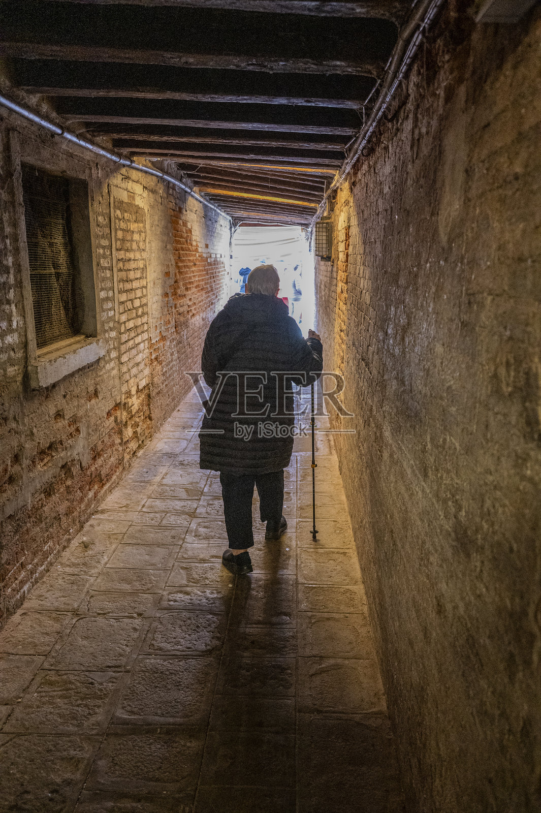 一位拄着手杖的老妇人在意大利威尼斯的街道上探索。照片摄影图片