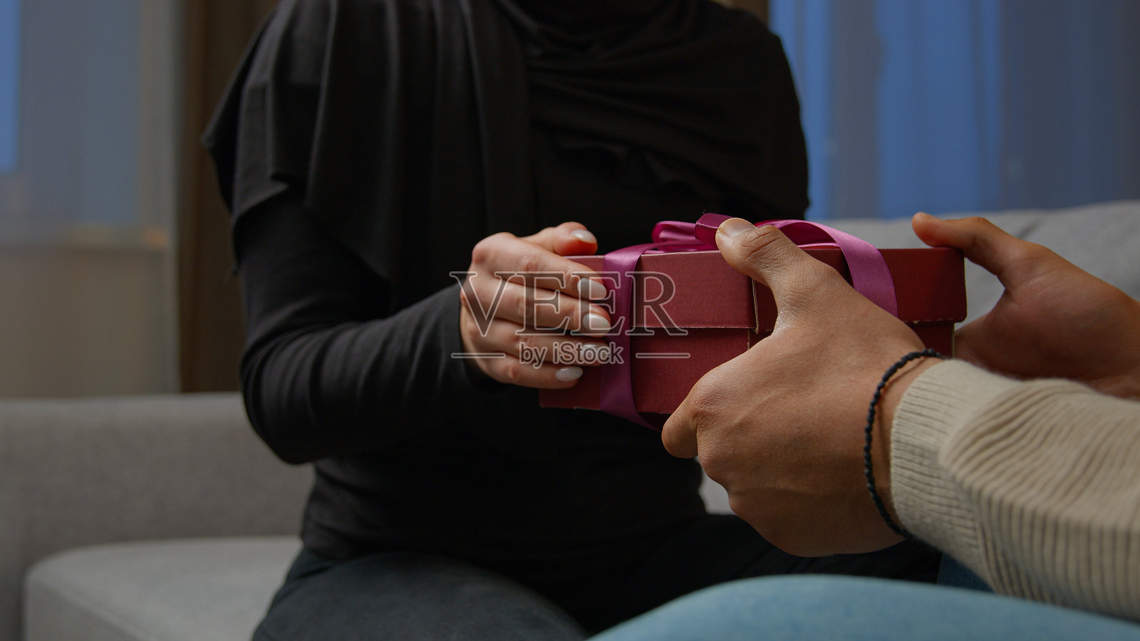 陌生男子祝贺心爱的女人，给她一个装有粉色丝带的惊喜礼盒，室内女性手中握着礼物，已婚家庭庆祝周年纪念、蜜月和情人节，象征着爱与亲情。照片摄影图片
