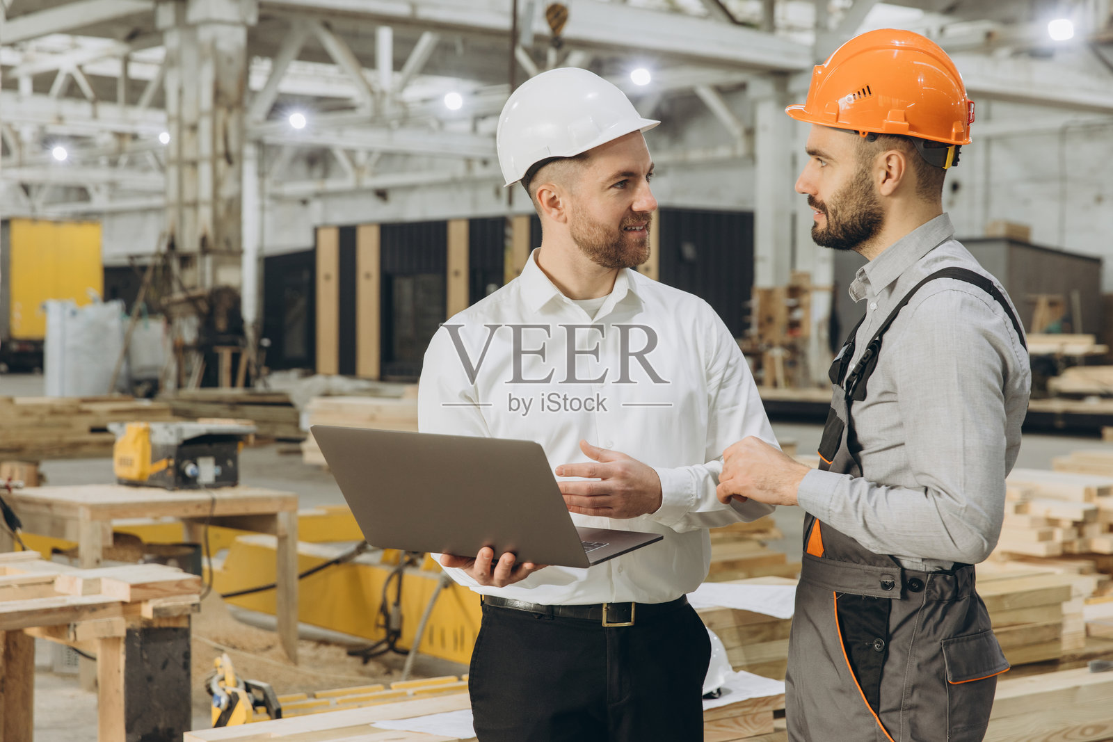 工程师在模块化建筑工厂讨论项目，使用笔记本电脑。照片摄影图片