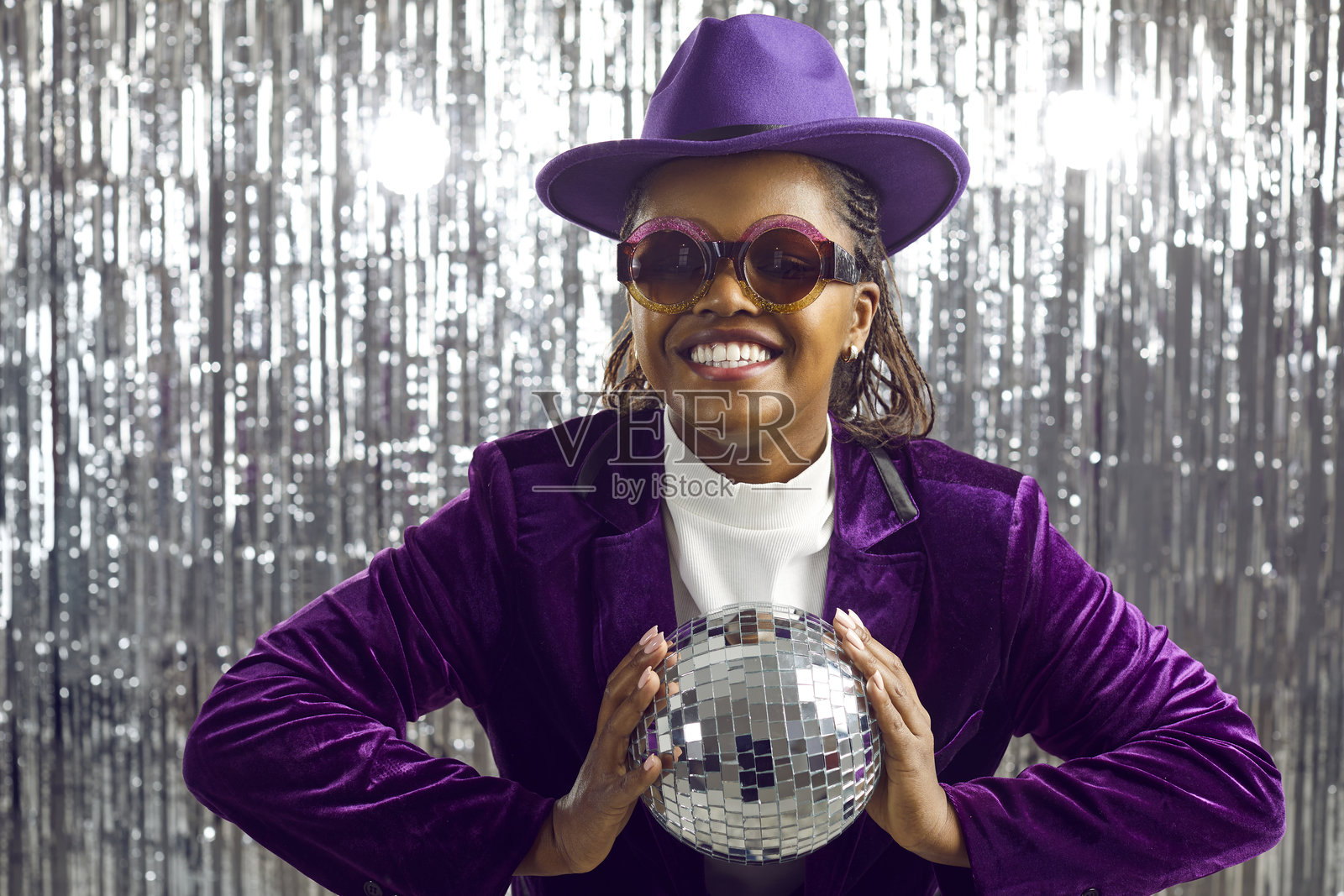 穿着天鹅绒西装的年轻深肤色女性双手托着迪斯科球。照片摄影图片