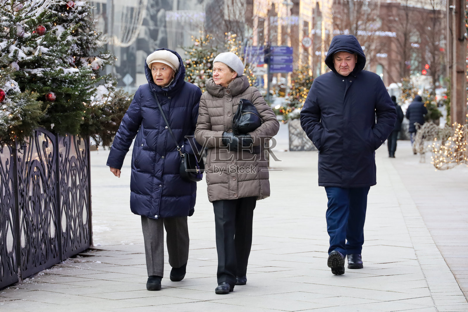 冬季背景下，老人在城市街道上走，身后是新年树木。照片摄影图片