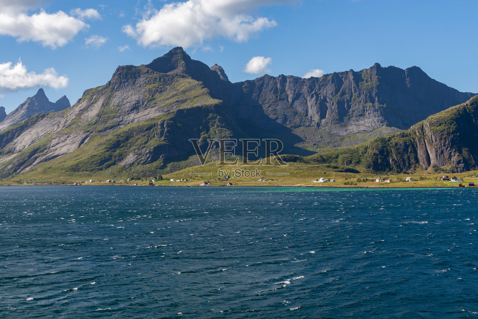 海岸线，深蓝色的海水，岸边有房屋，背景是高耸的绿色山脉照片摄影图片