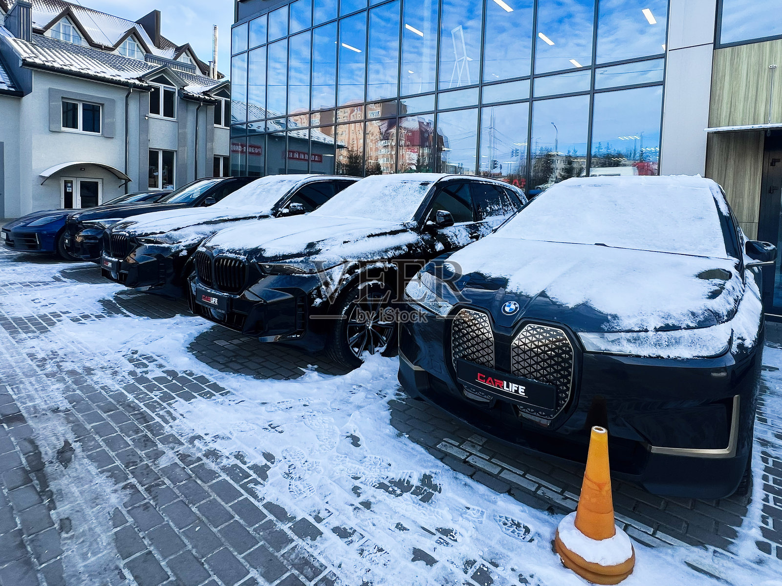 一排豪华的宝马汽车被雪覆盖,停靠在一座现代建筑附近照片摄影图片