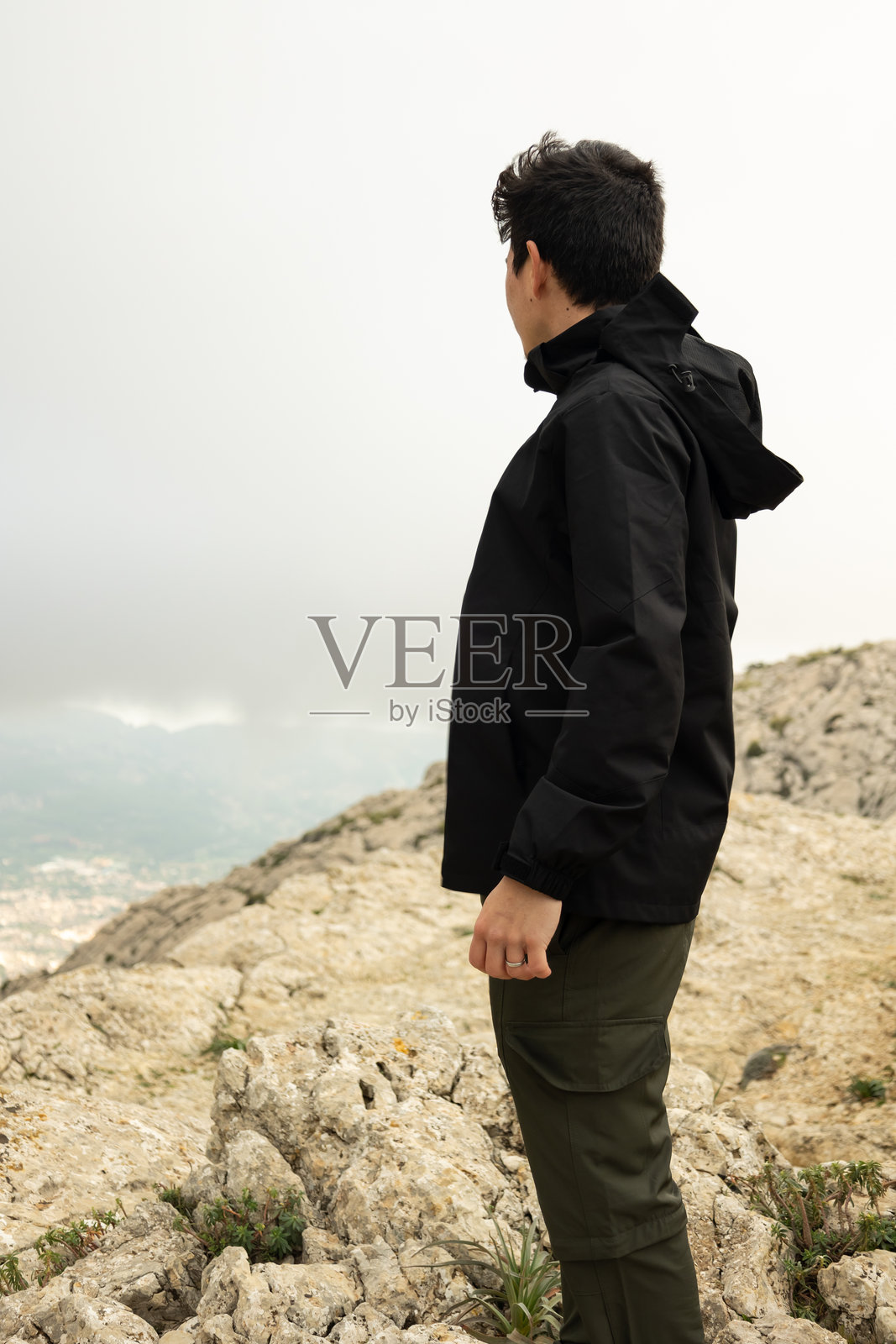 一名男子在雾蒙蒙的山顶俯瞰村庄的竖版图像照片摄影图片