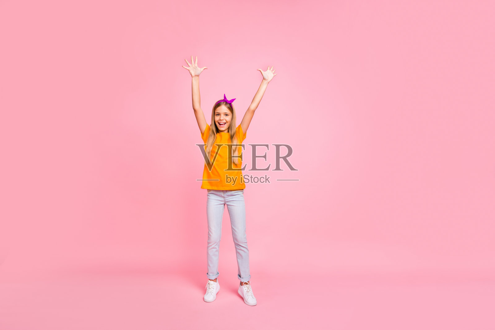 全身照，漂亮迷人的可爱阳光女孩，穿着黄色T恤，双手举起，享受乐趣，背景为粉色柔和色调。照片摄影图片
