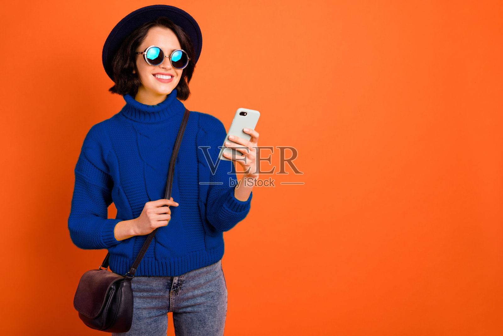 现代奢华的漂亮女友在橙色背景下独自浏览手机，寻找促销和折扣，面带愉悦的笑容。照片摄影图片