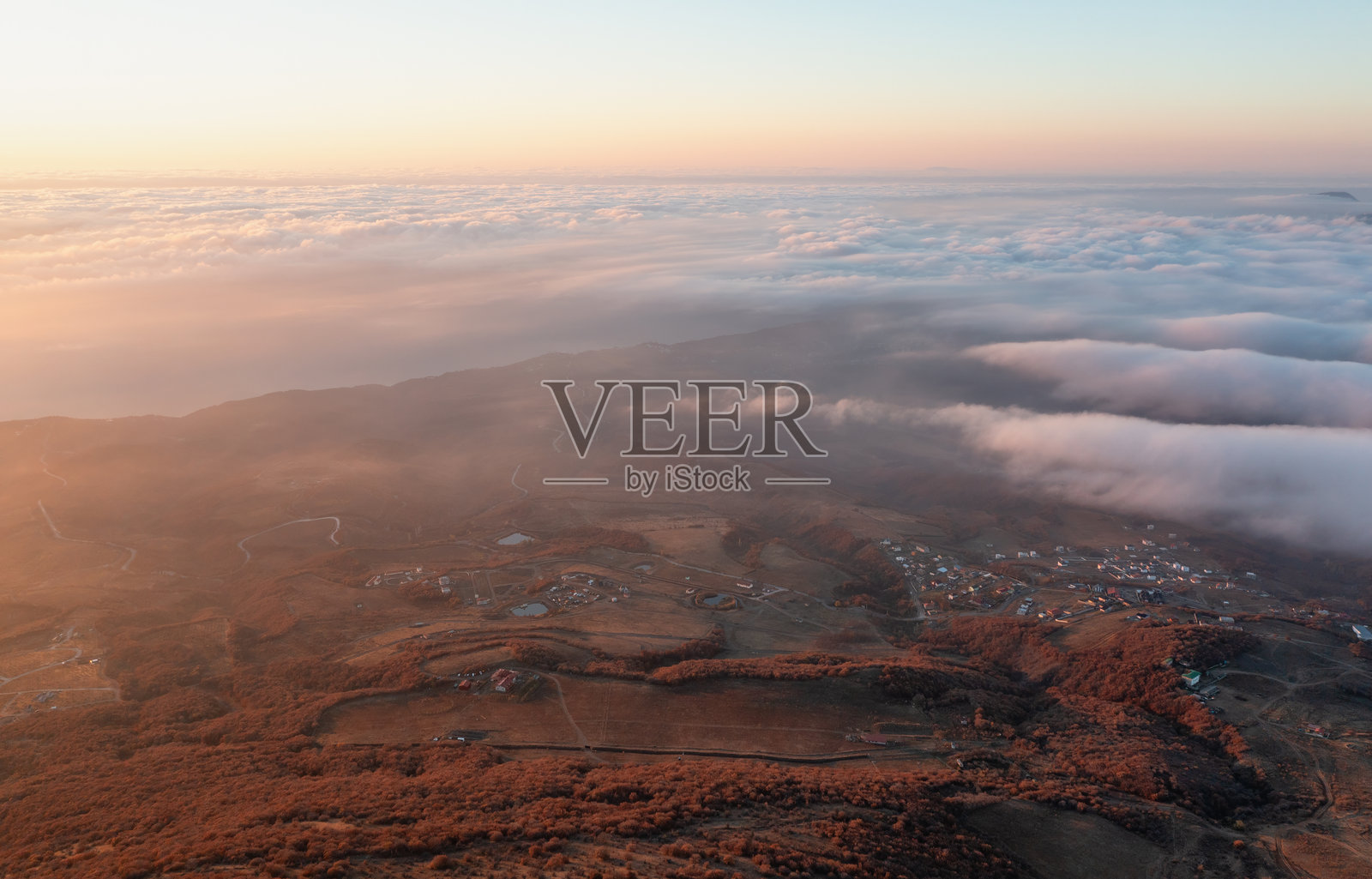 日出时分，云雾环绕的山丘和小村庄的鸟瞰图照片摄影图片