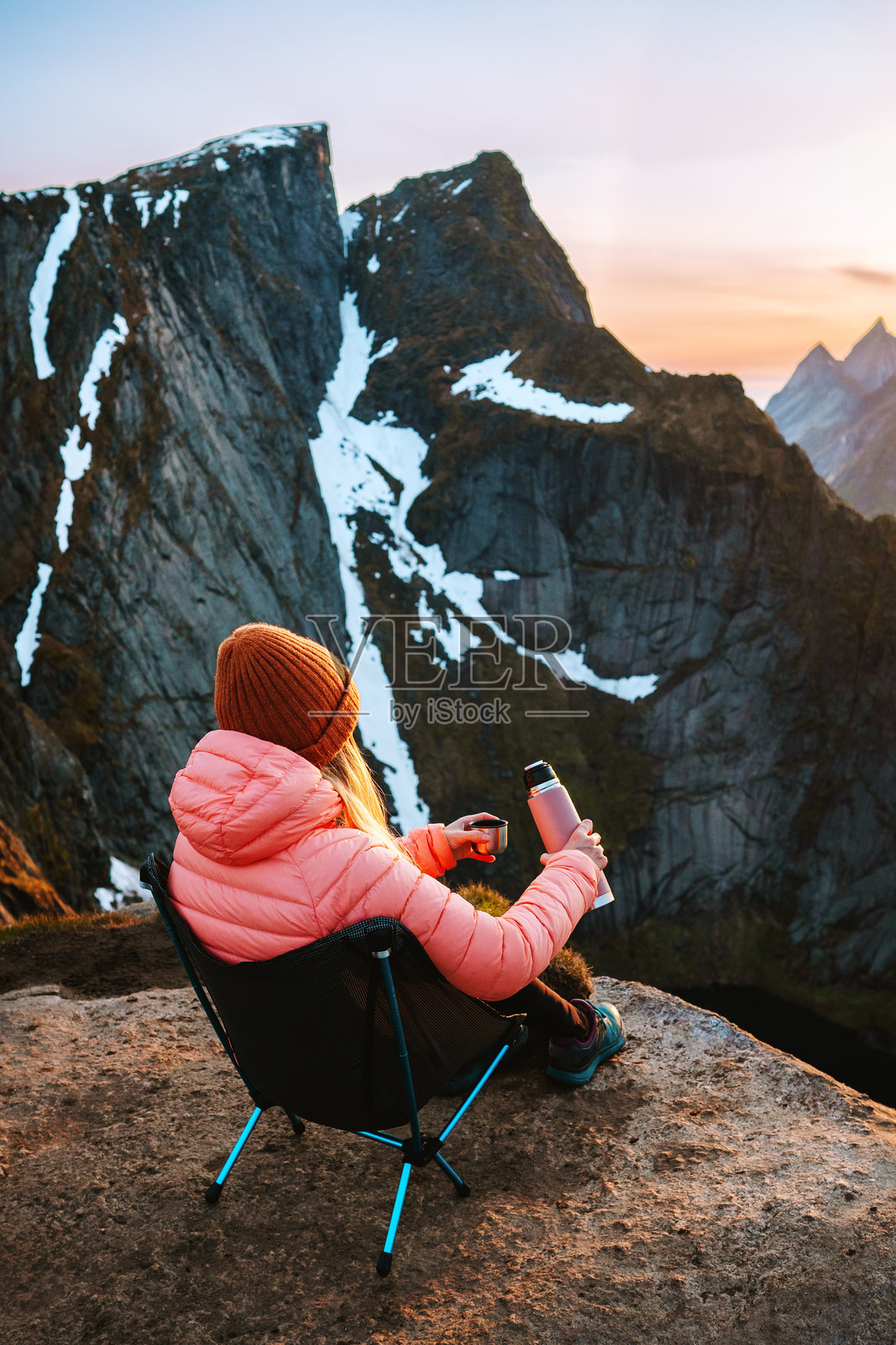 在挪威的山中，女冒险者坐在露营椅上放松，手里拿着保温瓶，独自徒步旅行，欣赏洛弗敦群岛的美景，享受积极的假期和健康的生活方式。照片摄影图片