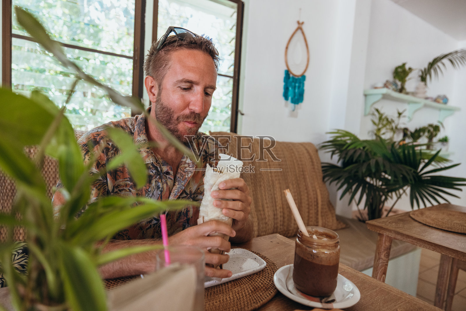 男子在热带咖啡馆享受墨西哥卷饼和冰咖啡照片摄影图片