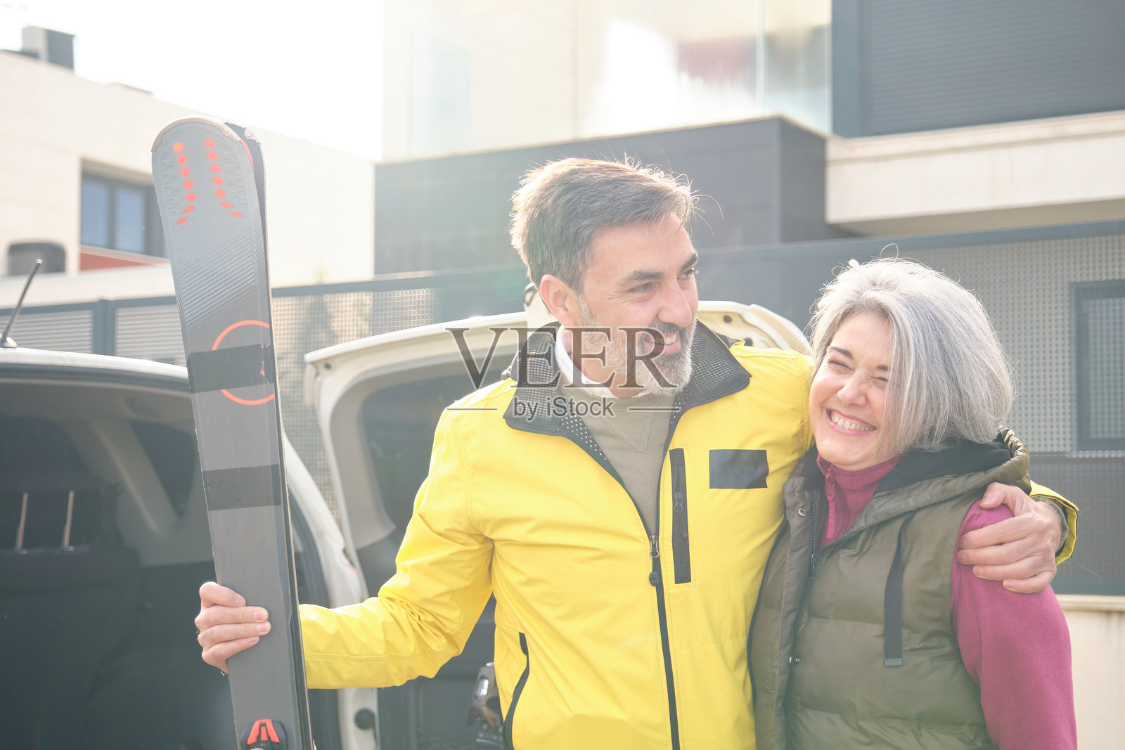 快乐的成熟夫妇正在为滑雪假期准备，将滑雪板装入汽车后备厢。照片摄影图片
