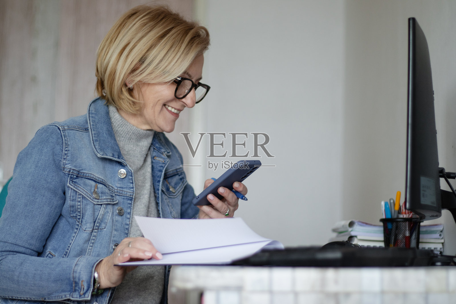 成熟的金发女性戴着眼镜，坐在桌子前，正在她的计划本中协调工作任务和开支。照片摄影图片