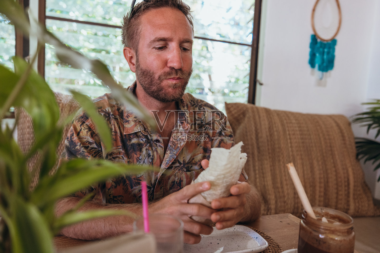 男子在热带咖啡馆享受墨西哥卷饼和冰咖啡照片摄影图片