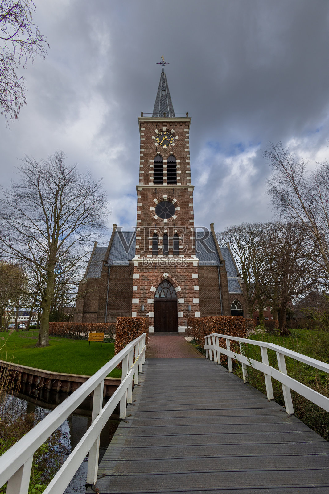一座风景如画的砖砌教堂，拥有高耸的尖塔，四周环绕着光秃的树木，从一座木栈桥上俯瞰。照片摄影图片