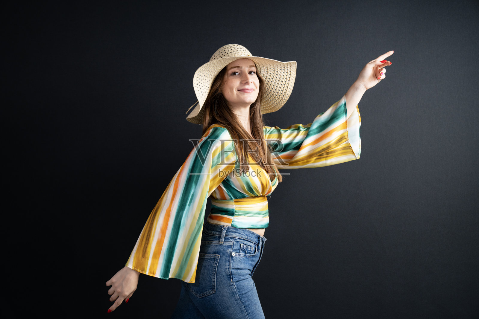 快乐美丽的年轻女性戴着草帽，站在黑色背景前照片摄影图片