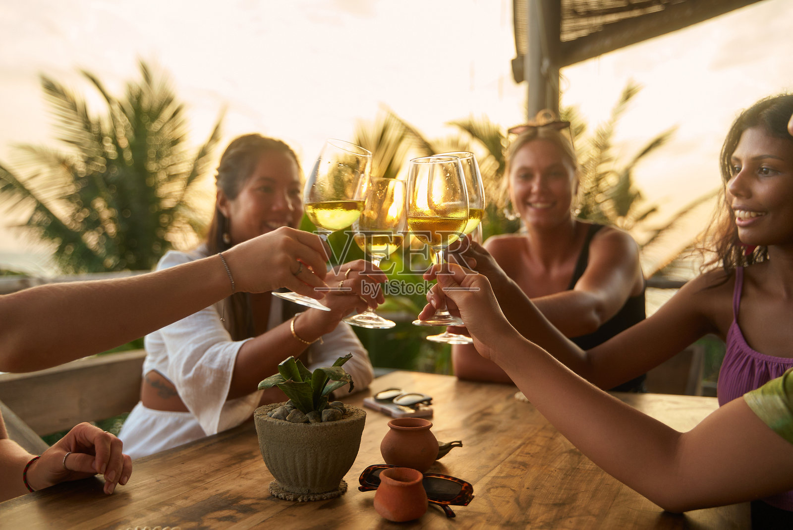 朋友们在阳光明媚的户外餐厅举杯庆祝。多元化的女性们庆祝单身派对之旅。轻松的氛围和愉快的聊天。时尚的环境，伴有棕榈树的美景。照片摄影图片