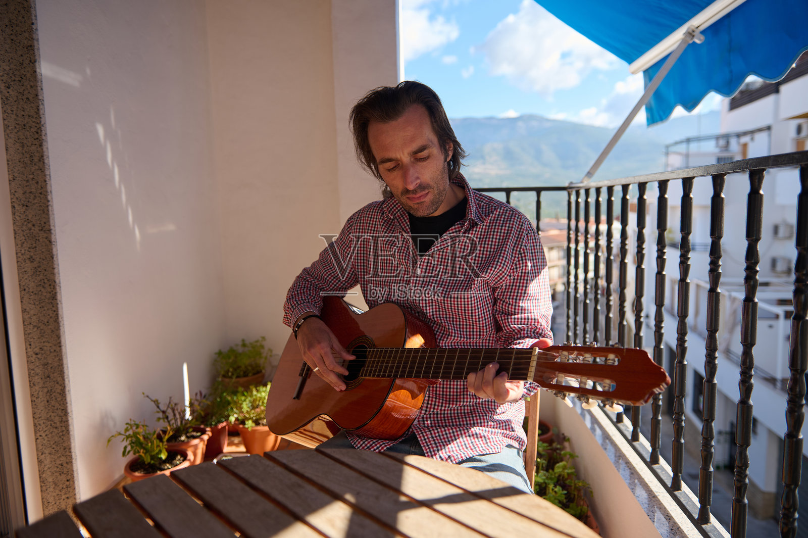 在阳光下的阳台上弹吉他的男人照片摄影图片