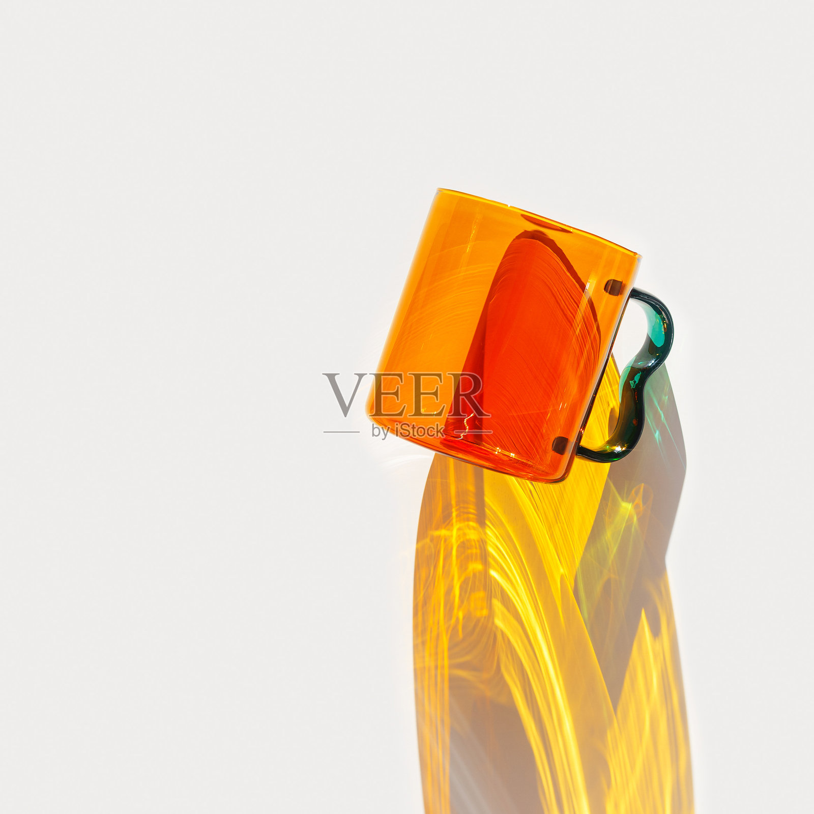 时尚的静物，橙色透明玻璃杯，闪亮的橙色茶杯或咖啡杯。阳光下动态的黄色阴影，白色表面的反射，极简美学设计，现代厨房，生动的色调。照片摄影图片