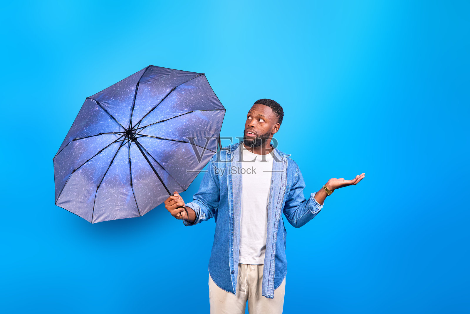 年轻男子手持雨伞，表情惊讶和困惑，手势表达。照片摄影图片