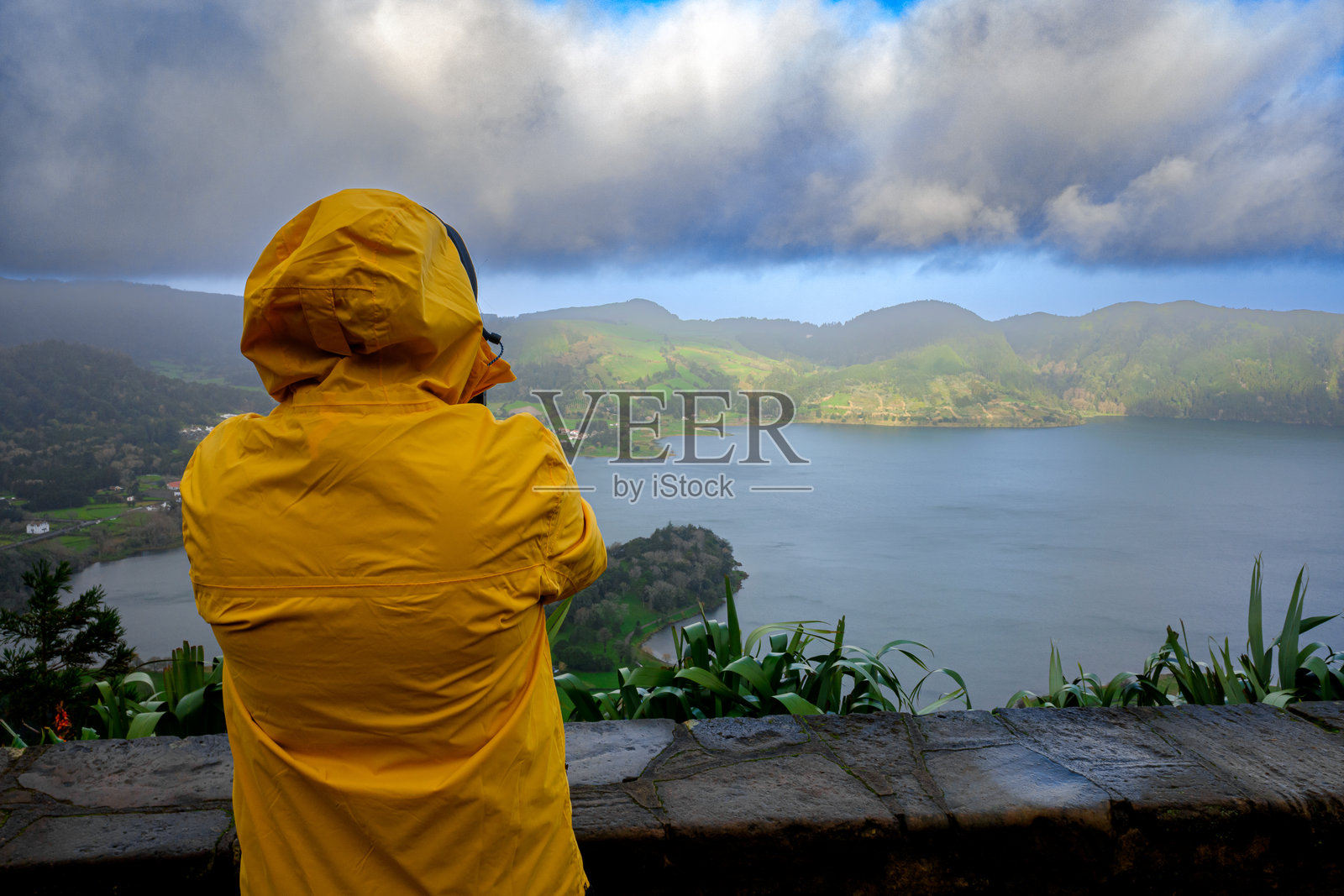 一位穿着黄色雨衣的女性仰卧，欣赏着葡萄牙亚速尔群岛圣米格尔岛的七城湖风景。照片摄影图片