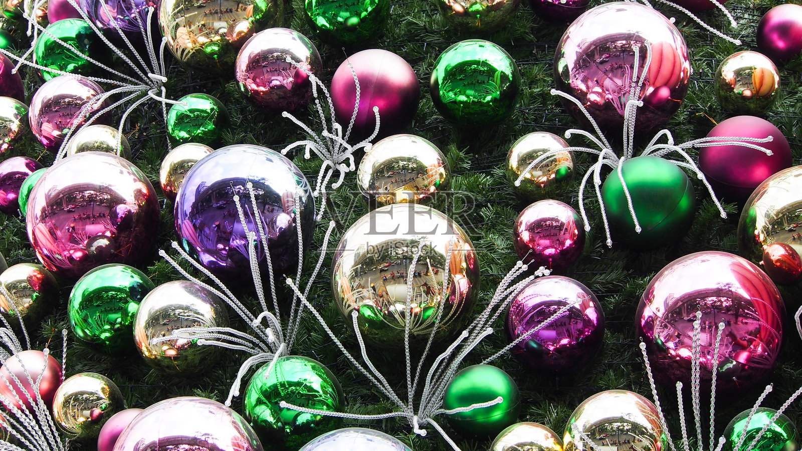 五颜六色的圣诞装饰品，包含粉色、绿色、金色和银色，排列在鲜艳的绿色背景上，营造出节日的热闹氛围。照片摄影图片