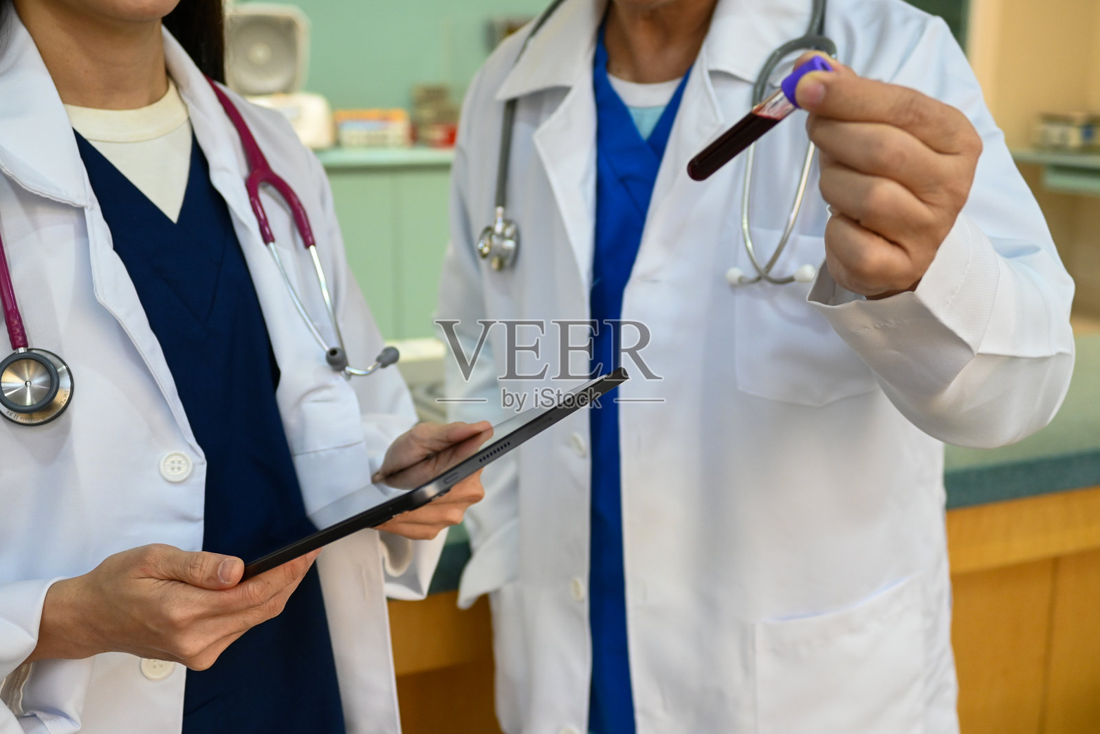 两位穿着白大褂和听诊器的医生正在使用平板电脑讨论患者的病史。照片摄影图片