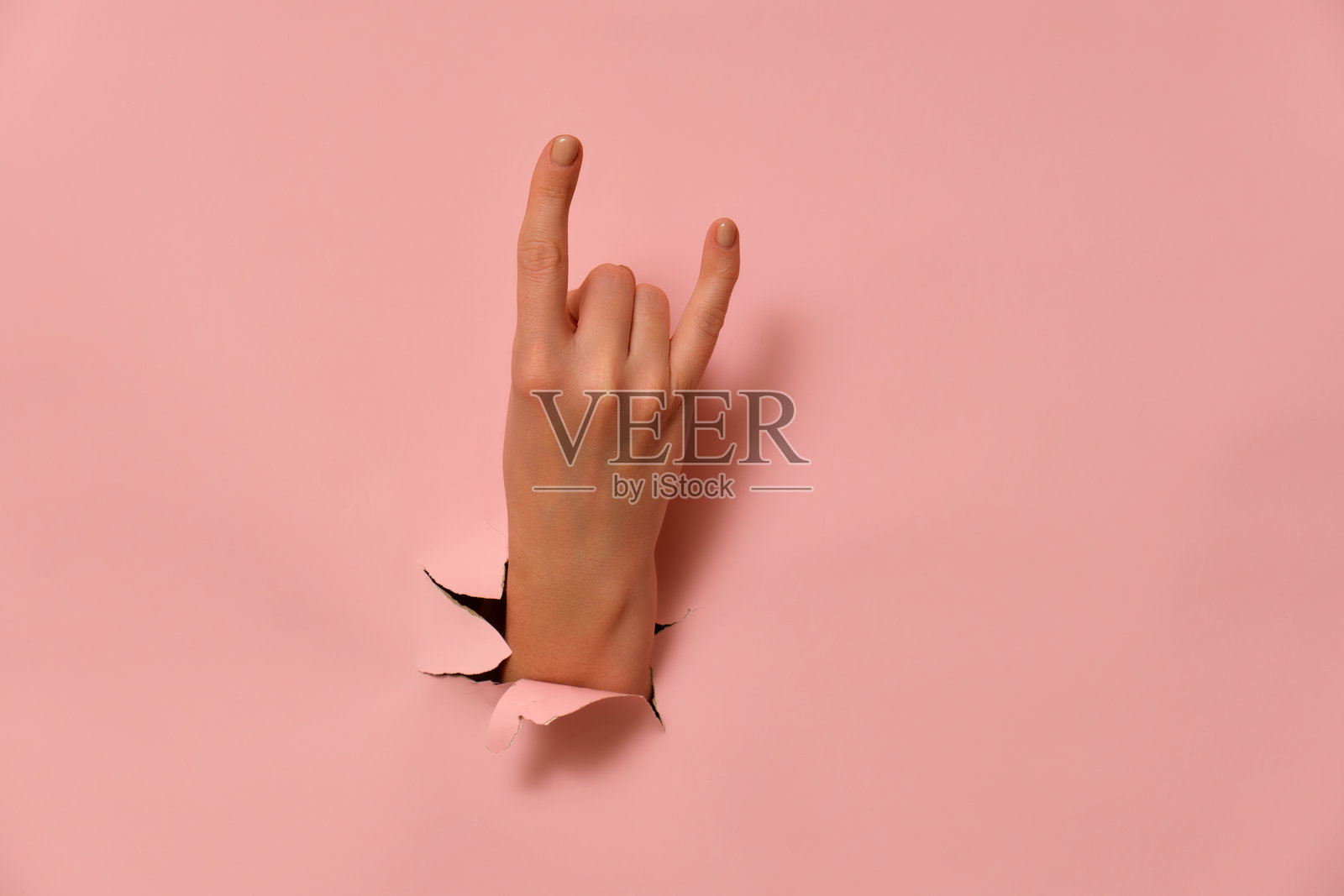 通过撕开的粉色纸张做出摇滚手势。极简创意摄影，留有空白空间。音乐与摇滚文化概念。适用于海报、横幅、贺卡和邀请函的设计。照片摄影图片