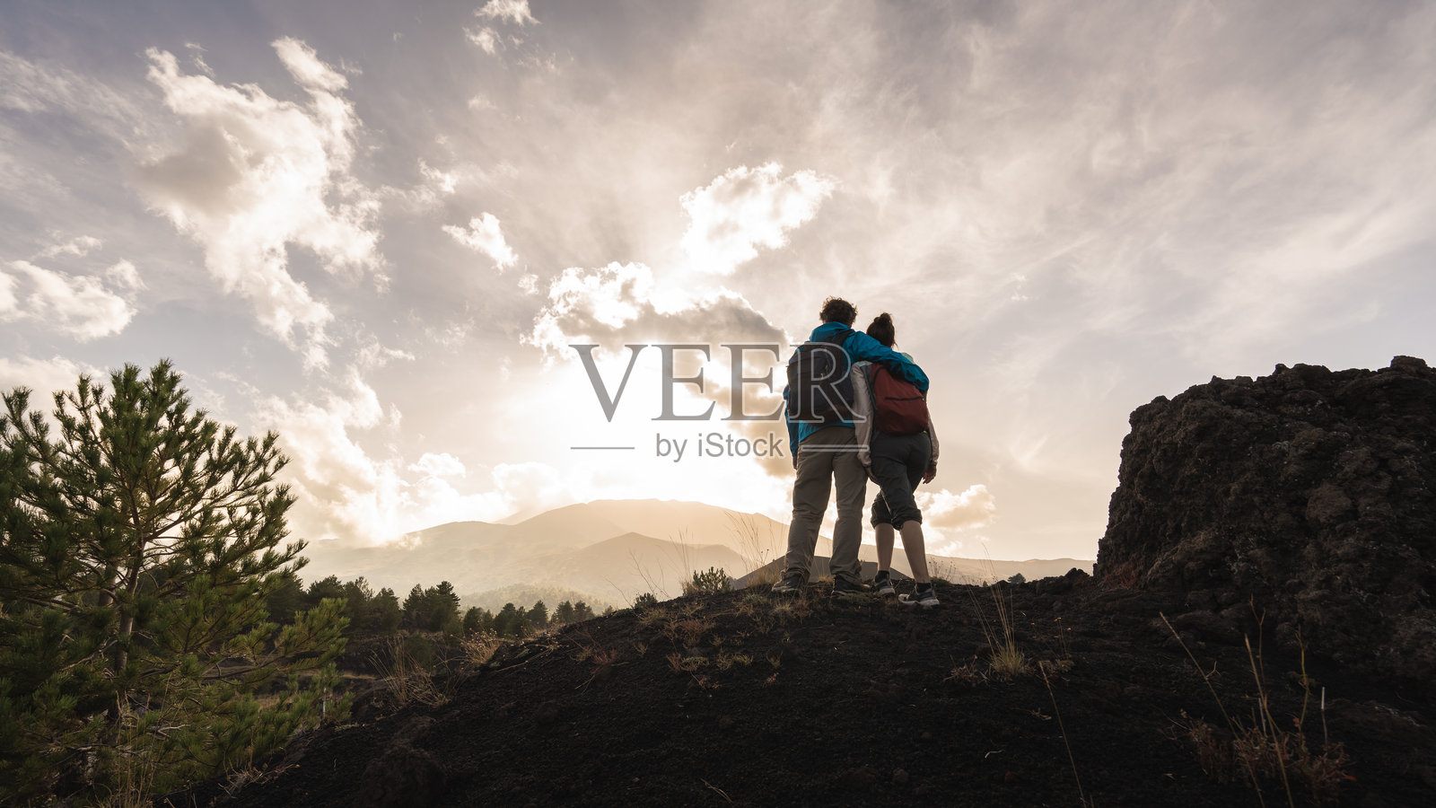 情侣在火山峰上欣赏山景，共同享受日落冒险。照片摄影图片