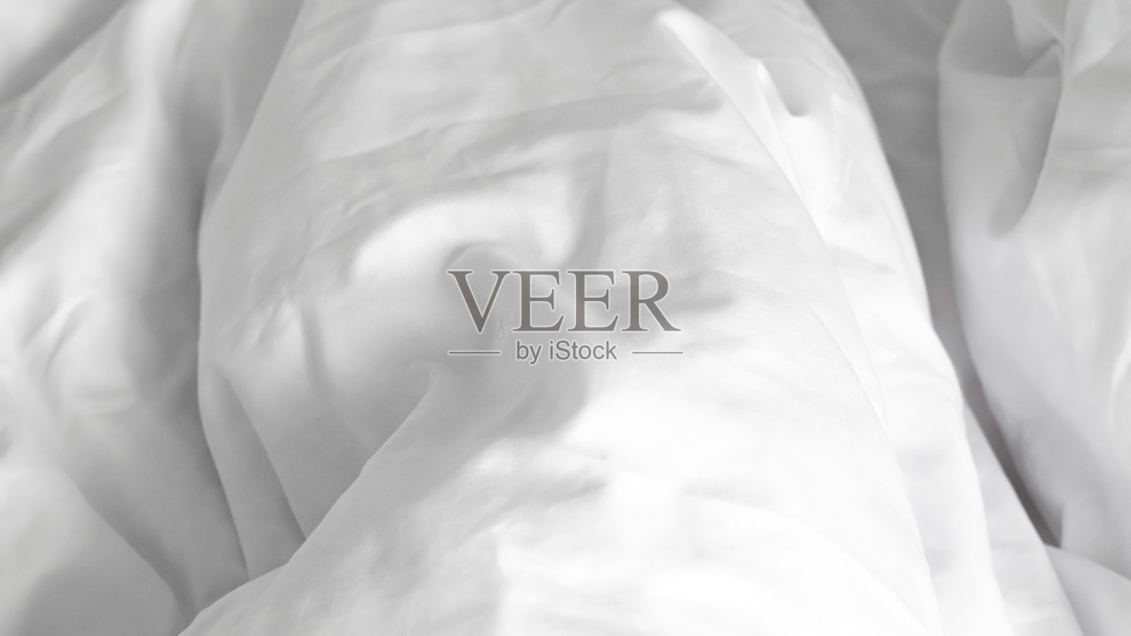 柔软蓬松的白色床单铺在未整理的床上，突显极简设计。照片摄影图片