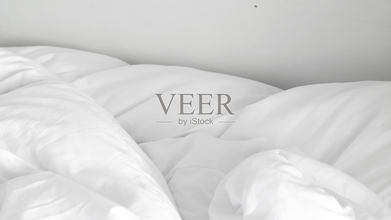 柔软蓬松的白色床单铺在未整理的床上，突显极简设计。照片摄影图片