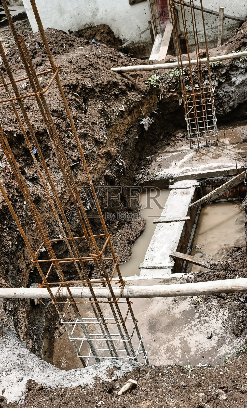 农村环境中明亮阳光下，住宅建筑的基础挖掘，配有钢筋和泥泞的坑。照片摄影图片