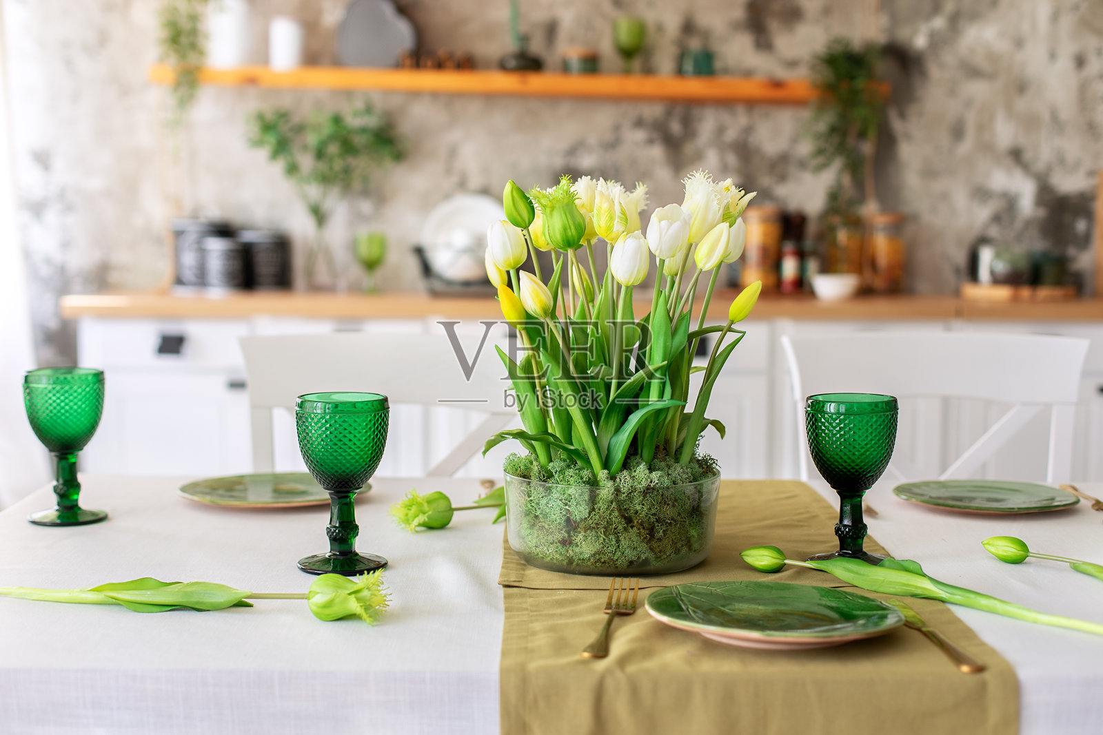 节日春季桌面布置，玻璃花瓶中插满郁金香和稳定苔藓。婚礼桌面装饰。美丽的餐桌上铺有桌布，摆放着酒杯和盘子，位于客厅中。照片摄影图片