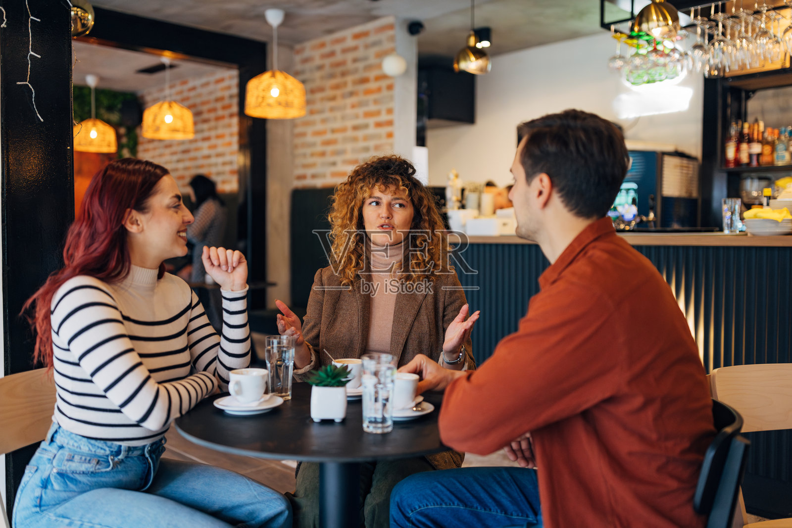 一群快乐的好朋友在咖啡店里一起享受时光。一群人在咖啡店里聚会。一男一女坐在咖啡桌旁，面带微笑。照片摄影图片