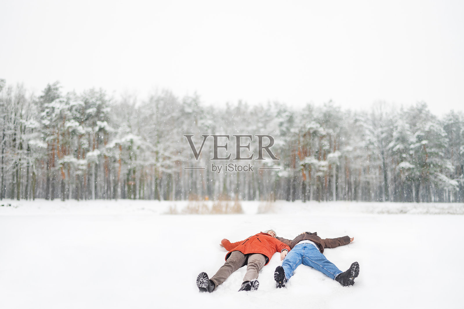 一对恩爱情侣在雪覆盖的森林中躺着玩耍照片摄影图片