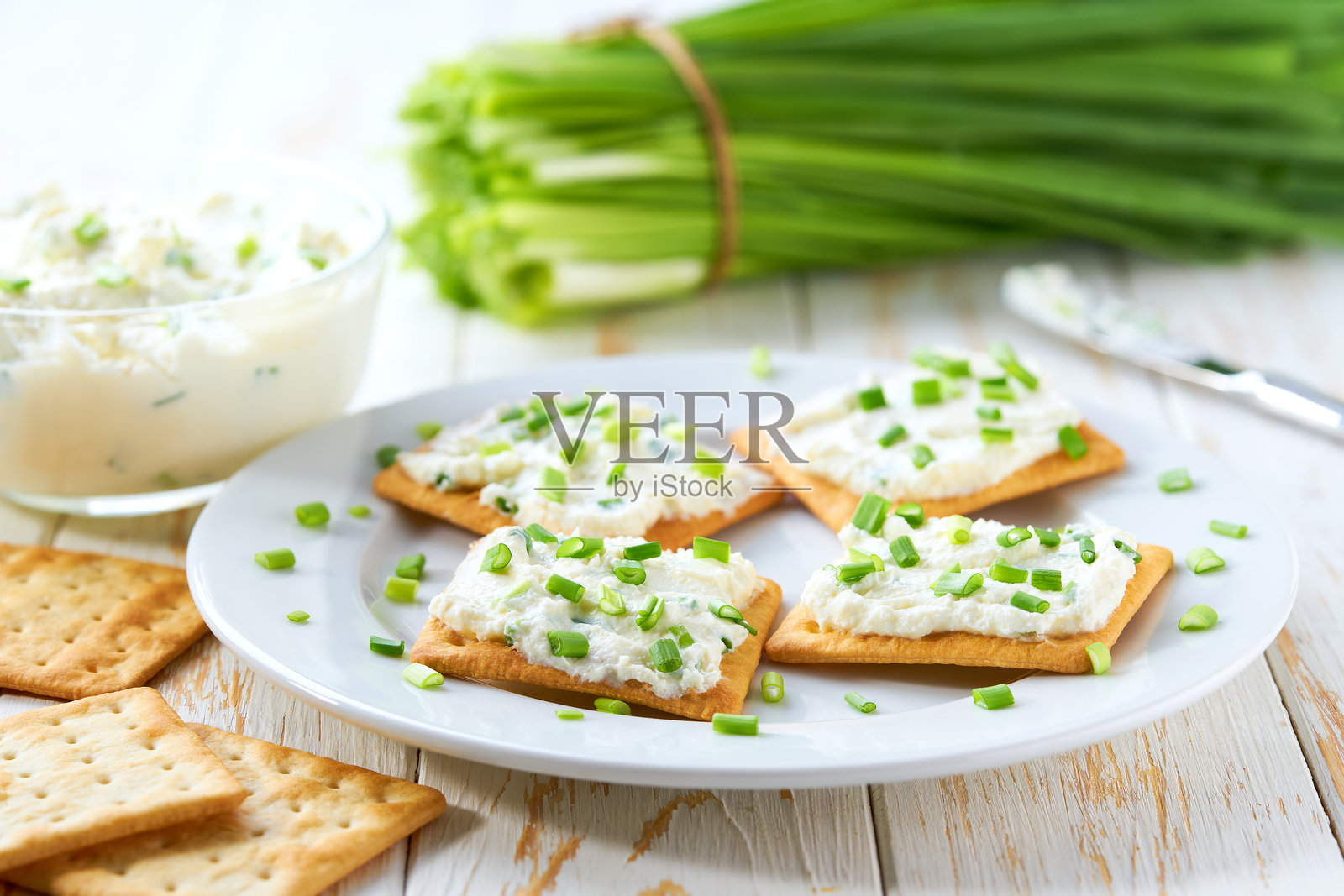 脆饼干和一个装有奶油奶酪涂抹酱及切碎细香葱的玻璃碗，放在明亮的厨房桌子上。照片摄影图片