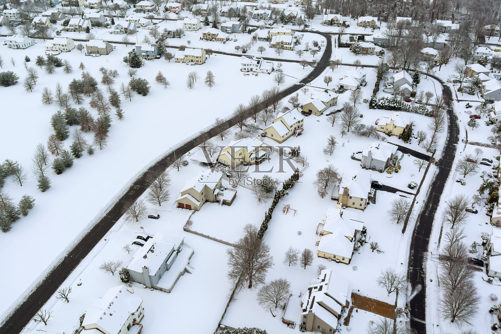被雪覆盖的美国郊区风景，建筑、道路和零散的树木清晰可见，展现出宁静的冬季氛围。照片摄影图片