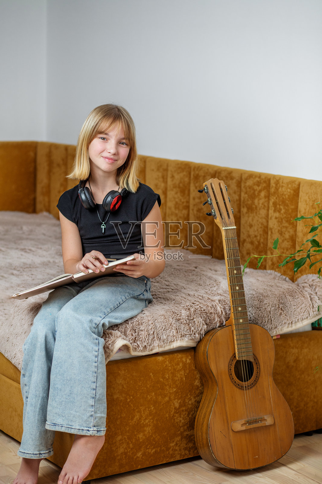 青春女孩在明亮的房间里，舒适的床上练习音乐，手里拿着吉他和笔记本。照片摄影图片