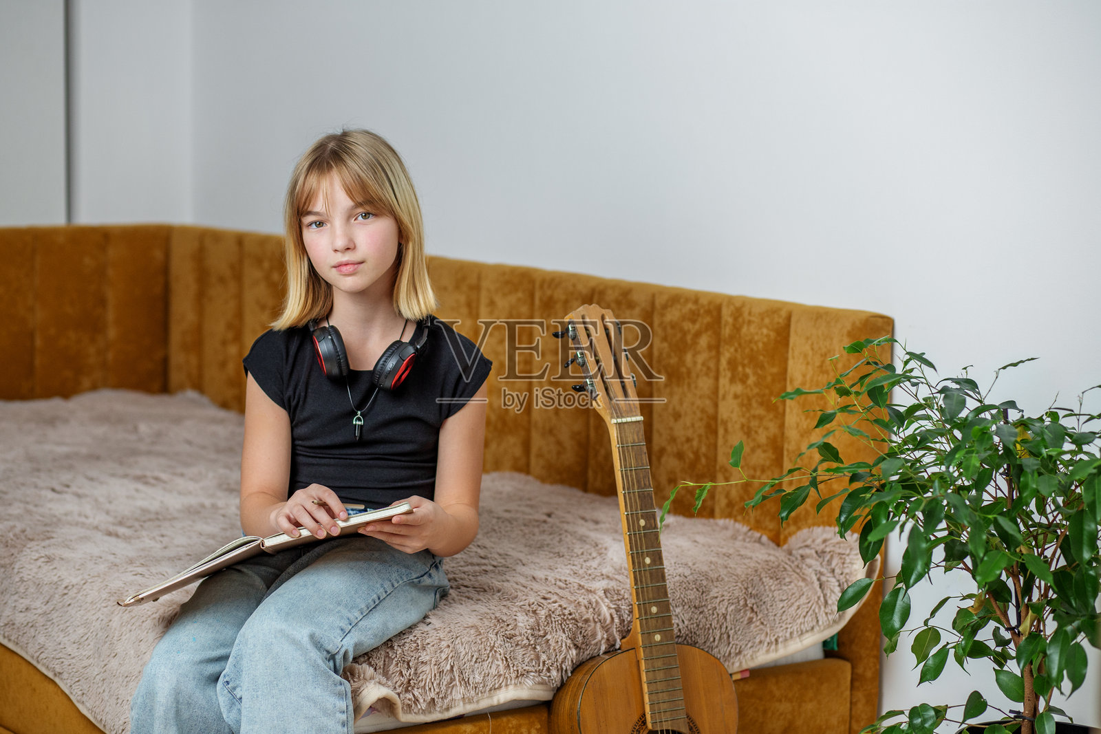 孩子坐在舒适的沙发上，探索音乐，身边有吉他和耳机。照片摄影图片