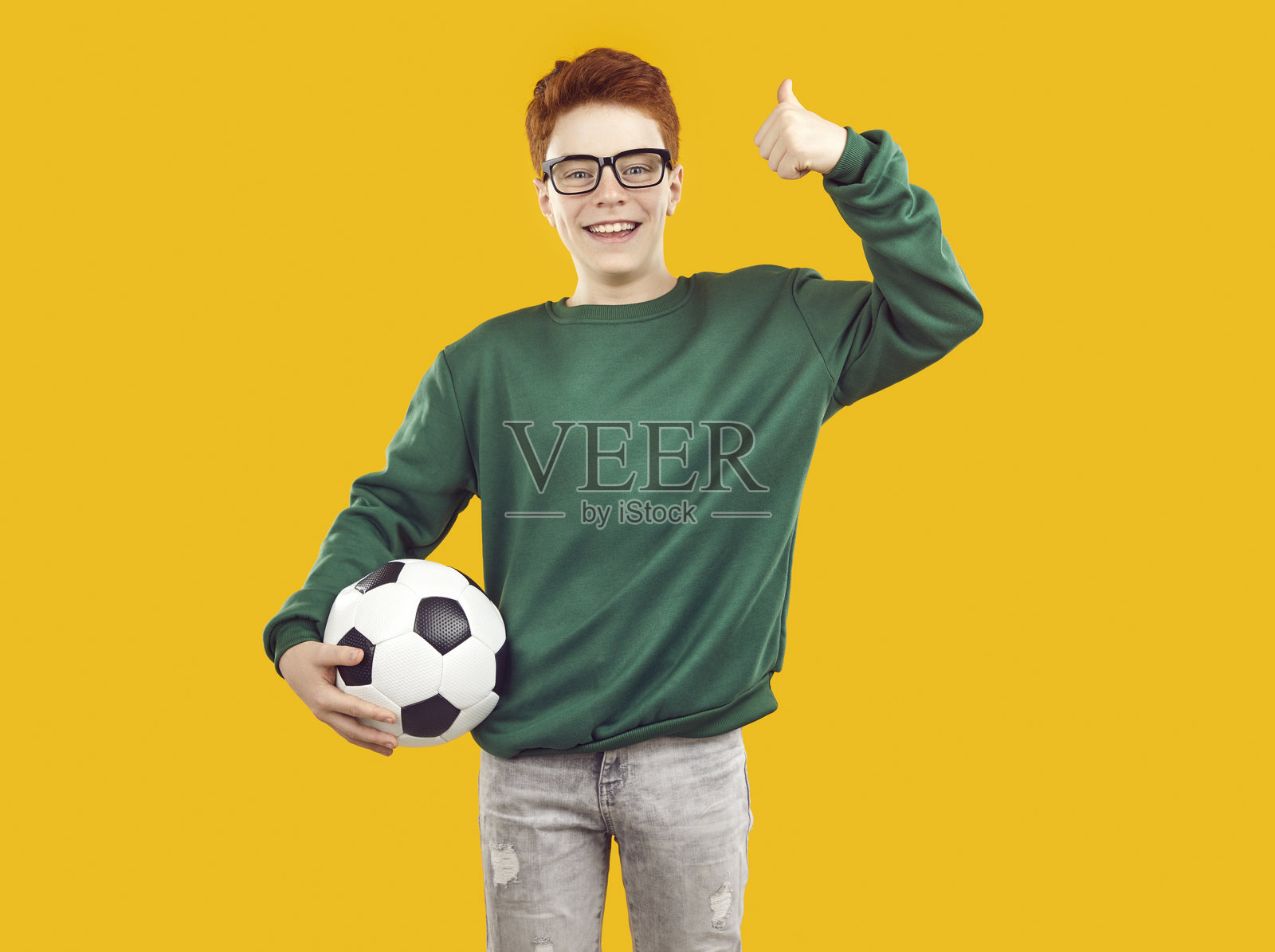 微笑、快乐的红发男孩在孤立的黄色背景上抱着足球。照片摄影图片