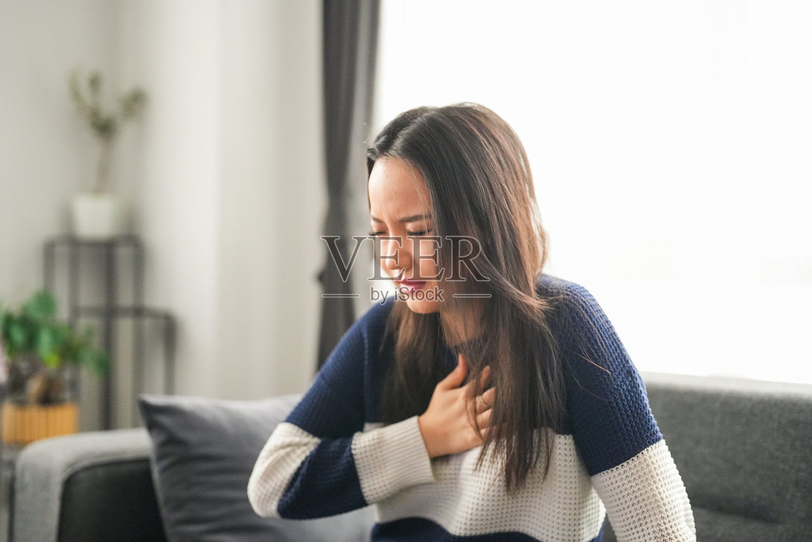 年轻女性坐在沙发上感到胸痛并咳嗽照片摄影图片