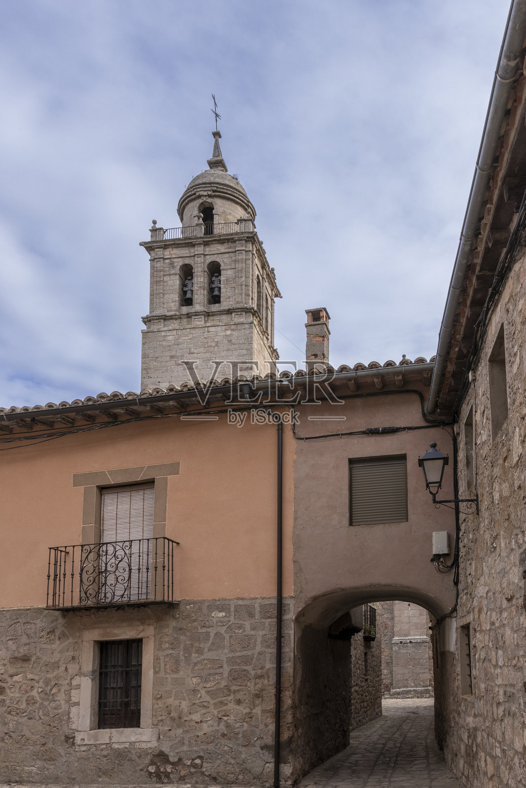 历史悠久的钟楼高耸于古朴村庄的石建筑之上，狭窄的拱形通道和乡村魅力在部分多云的天空下显得格外迷人。照片摄影图片