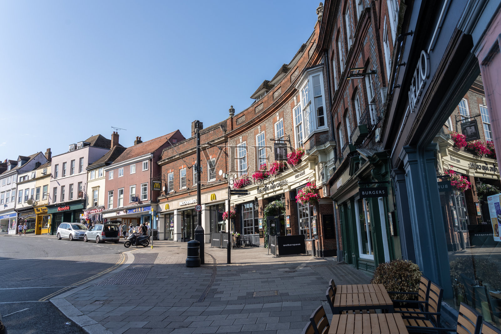 高街的下角，临近温莎城堡，街道两旁是商店、咖啡馆、餐厅和酒吧，阳光升起，投下阴影在人行道和店面上。照片摄影图片