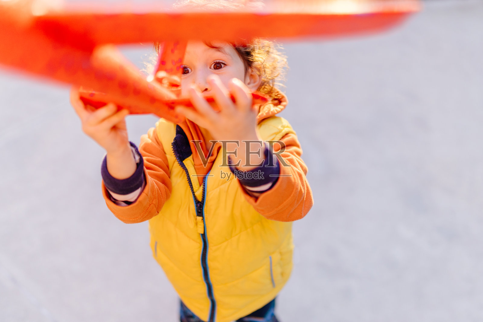 兴奋的孩子穿着黄色夹克，手里拿着橙色玩具飞机，看起来很满足。照片摄影图片